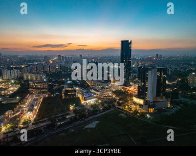 Vista aerea dei grattacieli che piangono il cielo crepuscolo, le loro luci rispecchiano il tramonto che svanisce sul paesaggio urbano, Golf Course Extension Road, Gurugram, Haryana, India. Foto Stock