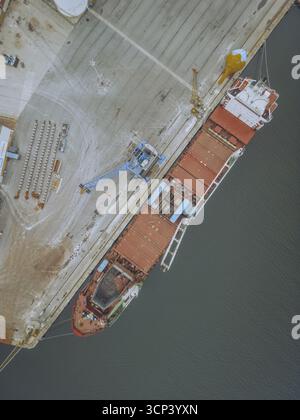 Vista aerea di una nave da carico arrugginita ormeggiata in un molo di cemento, il suo scafo rosso in contrasto con l'acqua scura, Viana do Castelo, Viana do Castelo, Portogallo. Foto Stock