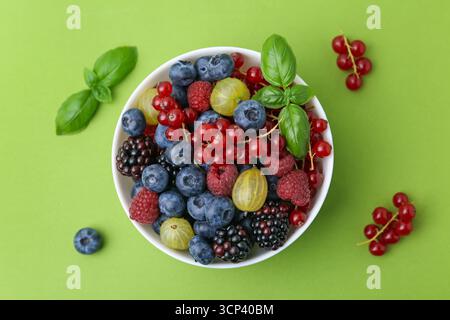 Diversi bacche mature e succose e basilico in ciotola su sfondo verde, piatto Foto Stock