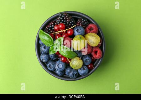 Diversi frutti di bosco e basilico maturi in ciotola su sfondo verde, vista dall'alto Foto Stock