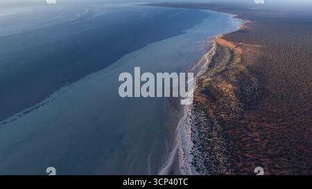 Vista aerea del punto d'incontro dell'oceano e della costa arida, dove le acque blu incontrano la terra rossa, creando un forte contrasto, l'Australia. Foto Stock