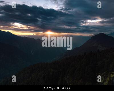 Veduta aerea dei raggi dorati del sole perforano le nebbiose nuvole scure, illuminando le aspre montagne boscose, Sosan, Himachal Pradesh, Indi Foto Stock