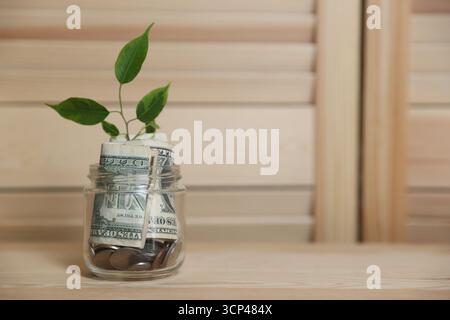 Vaso in vetro con germogli, monete e dollari su tavolo in legno, spazio per testo Foto Stock