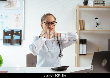 medico donna che ha un problema di salute soffre mal di collo problema causato duro lavoro. L'operatore sanitario ha lavorato troppo. Copia spazio Foto Stock