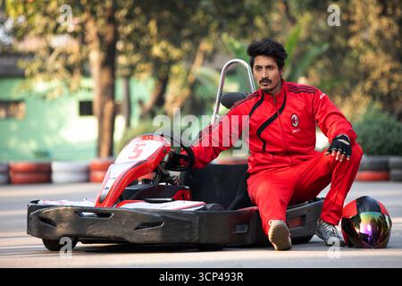 Un uomo concentrato in una tuta da corsa rossa seduto accanto a un go-kart Foto Stock