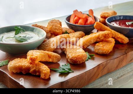 Pepite di pollo con verdure fresche e salse, ravvicinate su un tavolo di legno, con prezzemolo Foto Stock