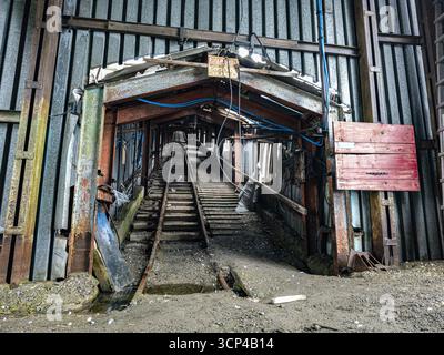 Vista dell'ingresso di una miniera in decadenza, con metallo arrugginito che incornicia un tunnel scuro e rotaie che scompaiono in lontananza, Pyramiden, Svalbard e Jan Mayen. Foto Stock