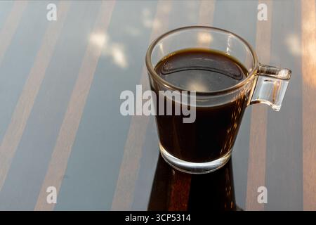 tazza di caffè nero in vetro su una superficie a strisce Foto Stock