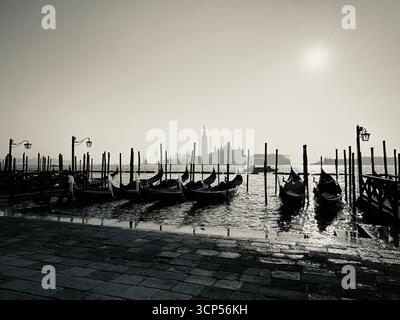 Vista di Venezia da Riva degli Schiavoni verso San Giorgio maggiore nel mese di dicembre il sole mattutino con gondole e lampade in bianco e nero Foto Stock