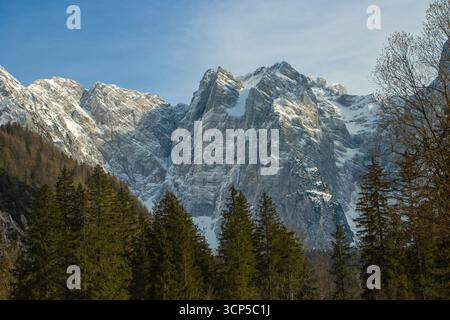 Vista panoramica del Monte Mangart dal Lago di Fusine nelle Alpi Giulie, mostrando maestosi paesaggi montani sotto il cielo blu. Foto Stock