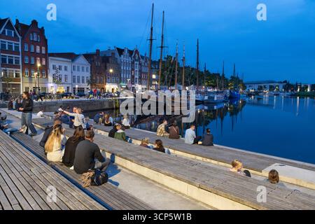 Persone sedute sulle scale d'acqua vicino al canale la sera, Lubecca, Schleswig-Holstein, Germania, Europa Foto Stock