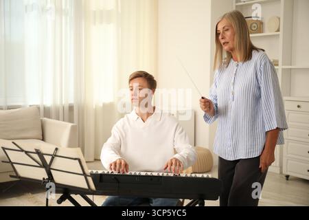 Tutore che insegna all'uomo a suonare il pianoforte al chiuso Foto Stock