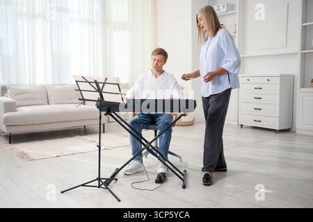 Tutore che insegna all'uomo a suonare il pianoforte al chiuso Foto Stock