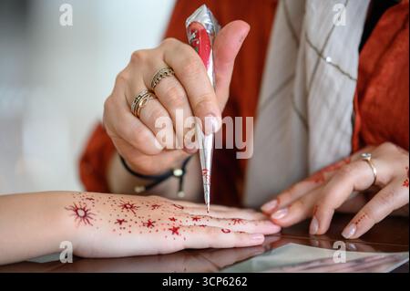 Il processo di applicazione del mehendi: L'artista fa un tatuaggio temporaneo all'henné sul braccio. Primo piano: Il maestro disegna l'henné sulla mano di una donna, tradizionale Foto Stock