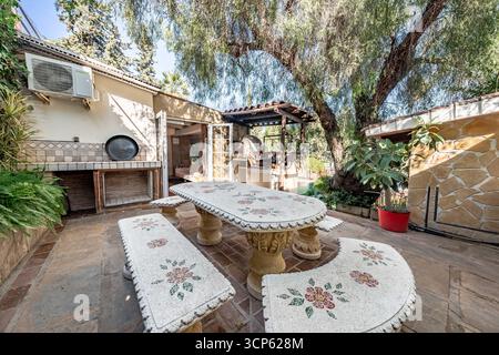 Area pranzo con patio all'aperto con tavolo a mosaico e barbecue in una lussuosa casa per vacanze mediterranea Foto Stock