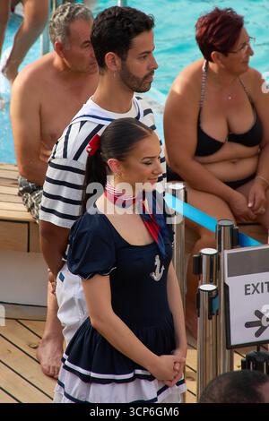 Venezia. Italia - 24 settembre 2025: Un intrattenitore maschile e femminile del team di animazione, vestito con costumi a tema marinaio, si erge sul ponte della piscina d Foto Stock