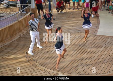 Venezia. Italia - 24 settembre 2025: Un cast di ballerini professionisti in costumi nautici esegue uno spettacolo vivace per i passeggeri sul ponte di legno di a c Foto Stock