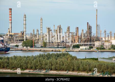Venezia. Italia - 24 settembre 2025: Un'estesa raffineria di petrolio e un impianto petrolchimico con numerose torri, tubi e fumogeni domina l'acqua Foto Stock