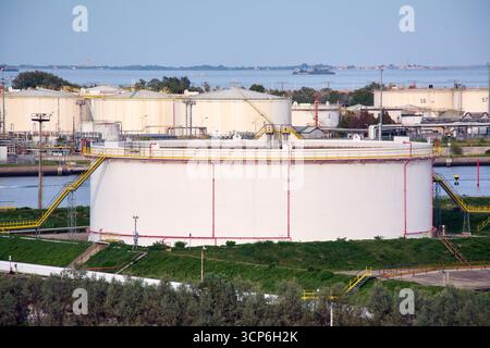 Venezia. Italia - 24 settembre 2025: Grandi cisterne cilindriche bianche si trovano presso un terminal di stoccaggio del petrolio sul lungomare, utilizzato per contenere il petrolio greggio Foto Stock