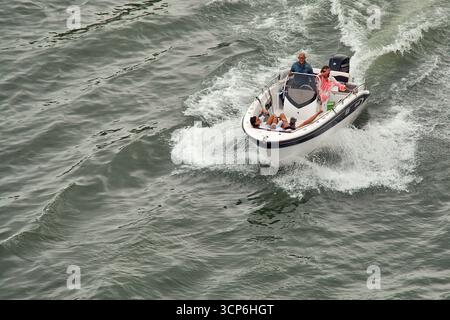Venezia. Italia - 24 settembre 2025: Un gruppo di quattro persone, tra cui un anziano che guida, goditi un viaggio di piacere su un motoscafo che attraversa il c Foto Stock