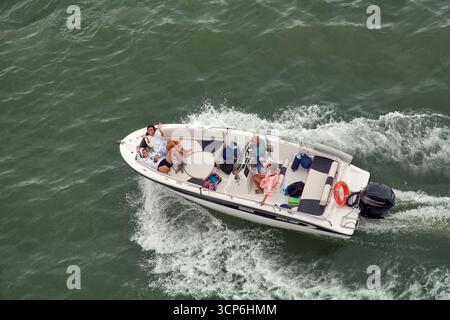 Venezia. Italia - 24 settembre 2025: Una veduta aerea mostra un gruppo di amici e un cane che si divertono su un motoscafo, con i passeggeri a prua che ondeggiano Foto Stock