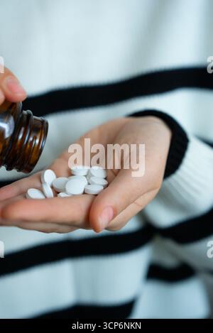 Persona che versa pillole bianche dalla bottiglia al palmo. Farmaceutica, medicina, concetto di trattamento. Foto Stock