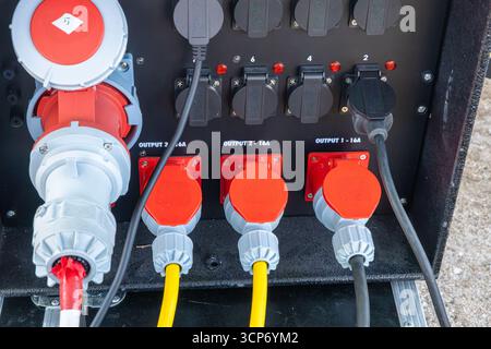 Primo piano di un quadro elettrico portatile con prese multiple, coperchi di sicurezza rossi e cavi gialli pronti per l'uso in ambienti esterni o sul campo. Foto Stock