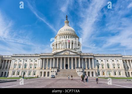 Edificio del Campidoglio DEGLI STATI UNITI Washington DC Stati Uniti | WASHINGTON D.C., Stati Uniti: I visitatori attraversano la piazza prima del fronte orientale del Campidoglio, dove la cupola e la Statua della libertà si innalzano contro un cielo luminoso punteggiato di nuvole. La costruzione del Campidoglio è iniziata nel 1793 e l'edificio è servito continuamente come luogo d'incontro del Congresso degli Stati Uniti fin dall'inizio del XIX secolo. Foto Stock