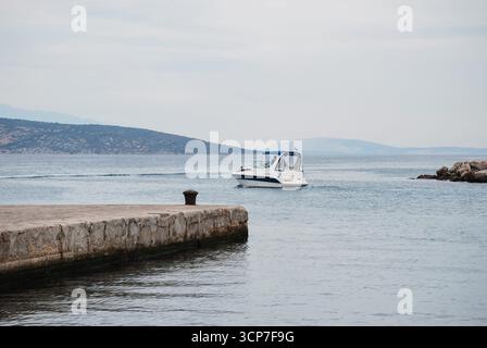 Krk, Croazia - 30 agosto 2012 - barca a motore che naviga nelle acque calme vicino alla costa rocciosa sotto il cielo nuvoloso. Foto Stock