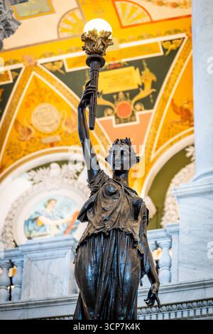 Jefferson Building Library of Congress Statue Washington DC // WASHINGTON DC — Una statua di bronzo con una torcia si trova in fondo alle scale nella Great Hall del Jefferson Building della Library of Congress. La statua è illuminata dalla luce della torcia che tiene in alto. Il Jefferson Building, l'edificio originale della Biblioteca del Congresso, è stato completato nel 1897 ed è rinomato per la sua architettura ornata e i murales decorativi. La Great Hall è uno spazio pubblico centrale all'interno dell'edificio, caratterizzato da colonne in marmo e intricate decorazioni a soffitto. Foto Stock