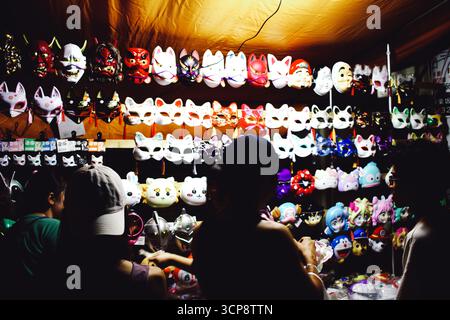 TOKYO, GIAPPONE - 20 settembre 2025: Un venditore vende maschere tradizionali e di carattere in uno stallo notturno del festival estivo illuminato. Foto Stock