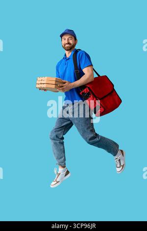 Corriere maschile con scatole per pizza che saltano su sfondo blu Foto Stock