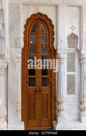 Porta ornata in legno intagliato con piano ad arco all'interno di un arco di marmo bianco Foto Stock