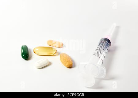 Pillole colorate e capsule accanto a una siringa. Un concetto per la vaccinazione, il diabete, le iniezioni, l'abuso di droghe o la scelta tra orale e iniettabile Foto Stock