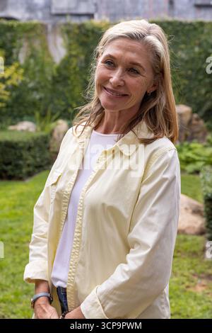 Donna anziana in piedi nel cortile posteriore che indossa una camicia gialla chiaro jeans blu con orologio da polso Foto Stock