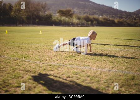Ragazzo in abbigliamento sportivo che strizza sul campo passando davanti a coni gialli vicino alla linea degli alberi al sole, copia spazio Foto Stock
