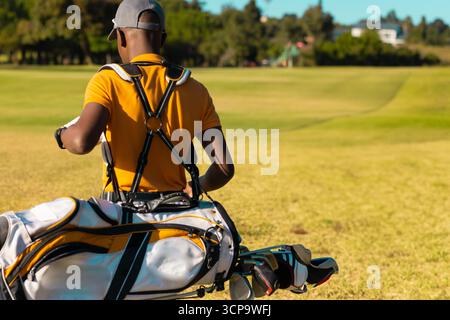 Golfista afroamericano che controlla l'orologio da polso sul campo da golf con borsa da golf e occhiali da sole, spazio fotocopie Foto Stock