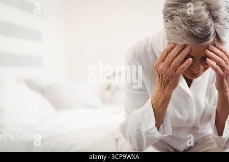 Pigiami bianchi a righe che avvolgono il bordo di un letto ben fatto nella camera da letto pallida, con piante in vaso Foto Stock