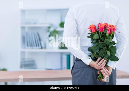 Uomo maturo in carica con bouquet di rose rosa-arancio dietro la scrivania, spazio per fotocopie Foto Stock