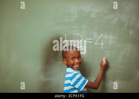 Ragazzo afroamericano che scrive problemi di sottrazione con il gesso sulla lavagna in classe, spazio di copia Foto Stock