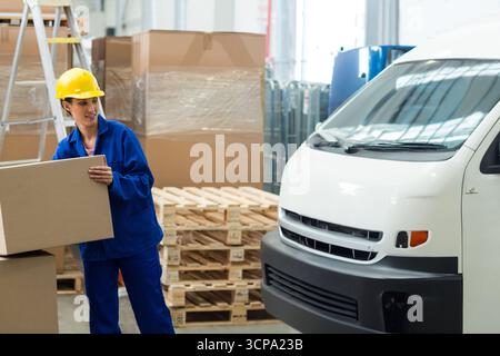 Scatola di cartone sollevata su pallet in legno all'interno del magazzino, con furgone bianco per consegne Foto Stock