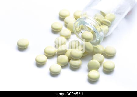 Le compresse gialle versano da una fiala di vetro su una superficie bianca in ambiente clinico Foto Stock