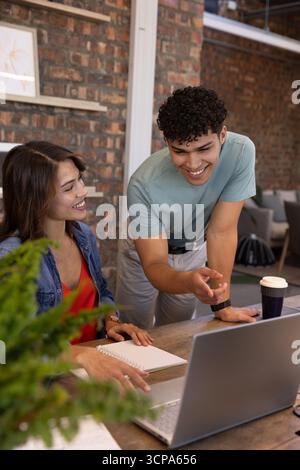 Diversi colleghi che collaborano alla scrivania in legno nello spazio di lavoro con computer portatile, notebook e tazza da caffè Foto Stock
