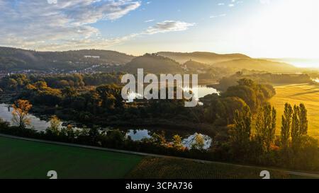 River Bend illuminato dal sole circondato da alberi d'autunno e Hillside Village Foto Stock