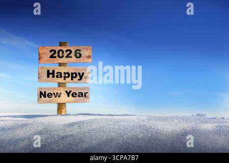 2026 FELICE anno nuovo scritto su un cartello di legno piantato nella neve contro un cielo blu Foto Stock