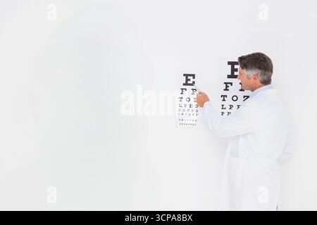 Optometrista maschio senior che punta con puntatore sulla mappa oculare Snellen nella sala esame oculare, spazio di copia Foto Stock