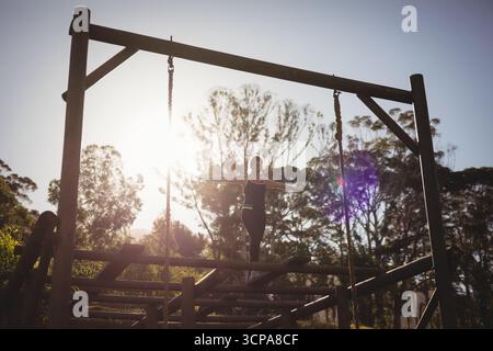 Donna in equilibrio su un fascio orizzontale di legno su un percorso ad ostacoli nella foresta, sole che crea luce parassita Foto Stock