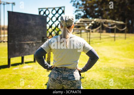 Membro di servizio donna che indossa un'uniforme mimetica in piedi sul campo che topografia percorso ad ostacoli al sole Foto Stock