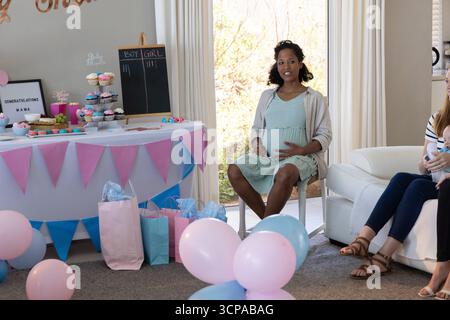 Diverse amiche che celebrano la doccia del bambino a casa con cupcake pastello, palloncini e lavagna Foto Stock