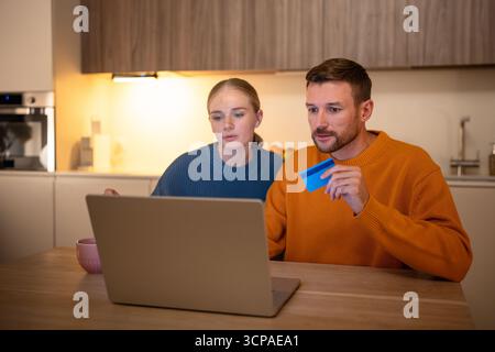 Marito e moglie premurosi stanno programmando un viaggio al tavolo con il computer portatile usando la carta di credito per il pagamento delle prenotazioni Foto Stock